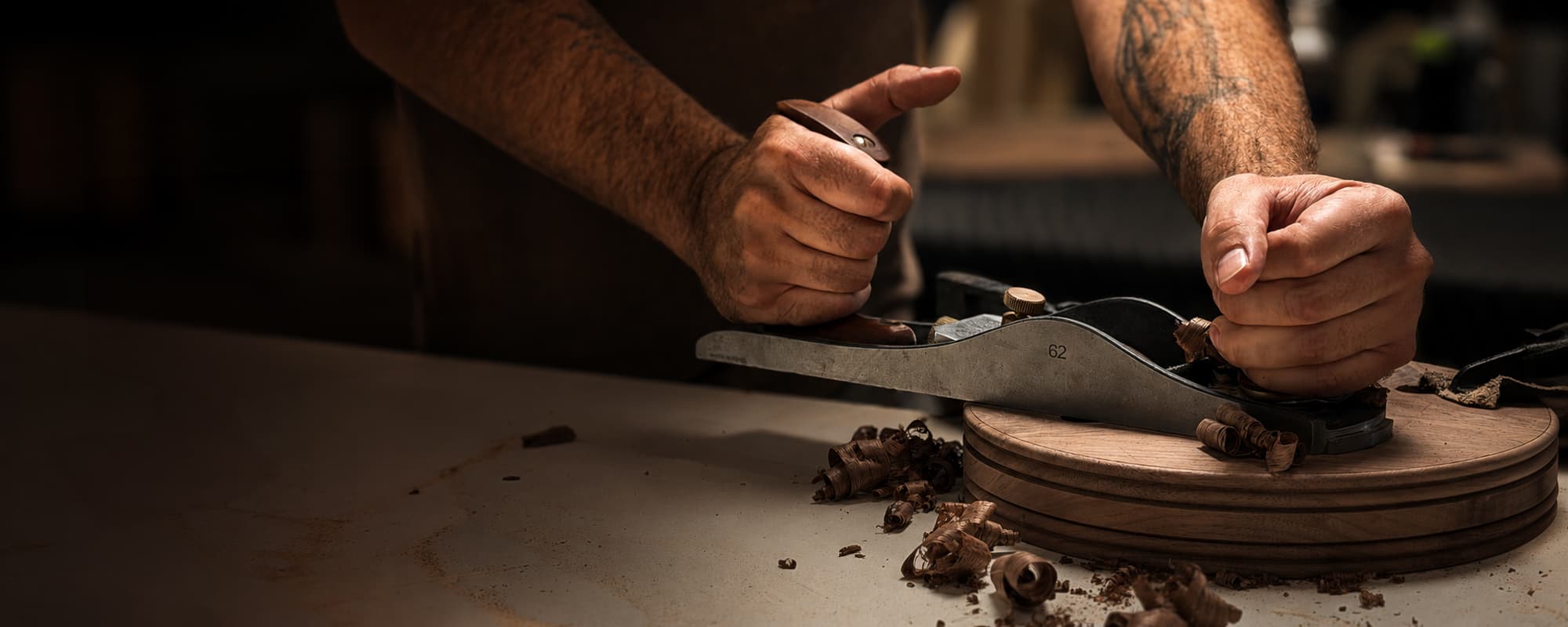 A maker smoothing a turned walnut piece with a hand plane at the workbench